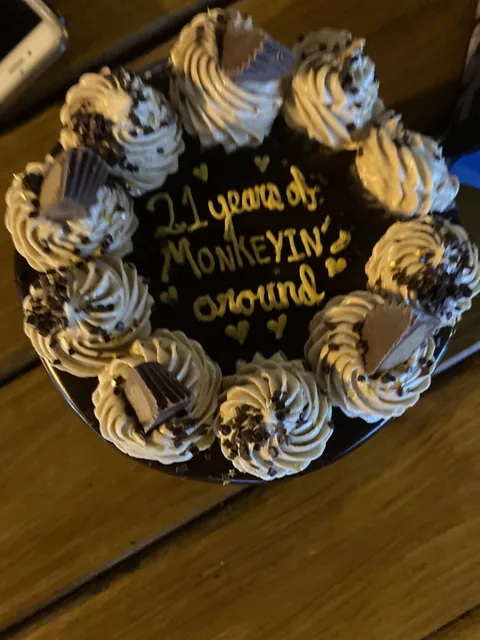Chocolate cake ringed with piped rosettes and peanut butter cups, lettered “21 years of monkeyin’ around.”