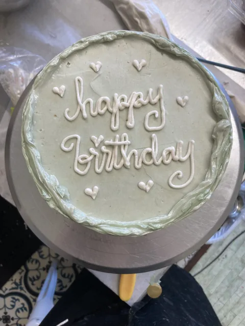 Sage green cake with white script reading “happy birthday” and small piped hearts.