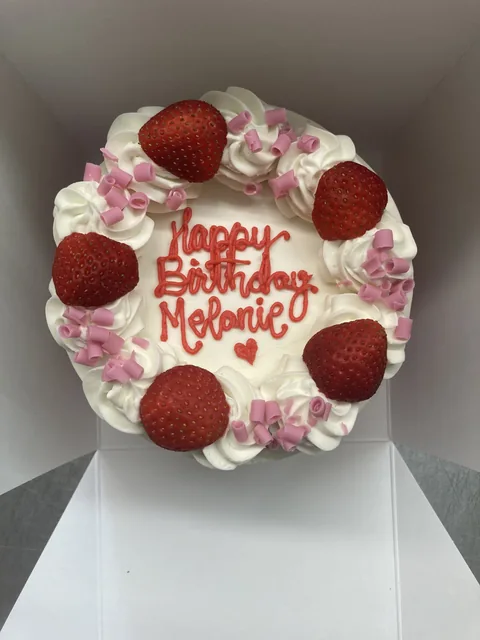 Round birthday cake piped “Happy Birthday Melanie” with fresh strawberries and pink candy pieces.