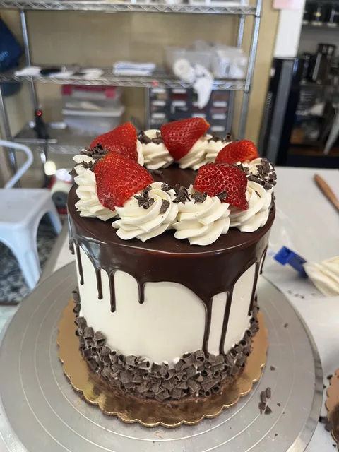 Tall white cake with a chocolate drip, whipped rosettes, fresh strawberries, and chocolate shavings.