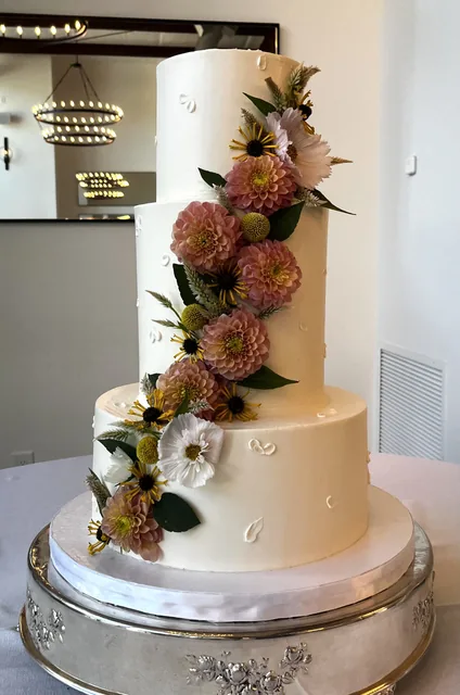 Three-tier white wedding cake with cascading dahlias and greenery.